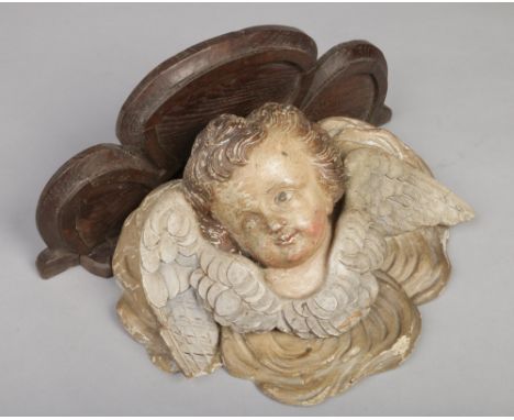 An 18th century Flemish polychrome carved corbel bracket. Modelled in the Baroque style as a putto and supporting a trefoil o