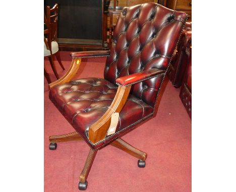 A contemporary mahogany and burgundy button leather and further brass studded Gainsborough swivel desk chair, on roller casto