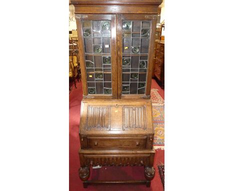 An early 20th century joined oak linenfold bureau bookcase, with twin colour lead glazed upper doors over fall front to two l