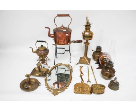 An assortment of metalware. Including a trivet stand with a wooden handle, a brass oil lamp, adjustable candlestick, a bevell