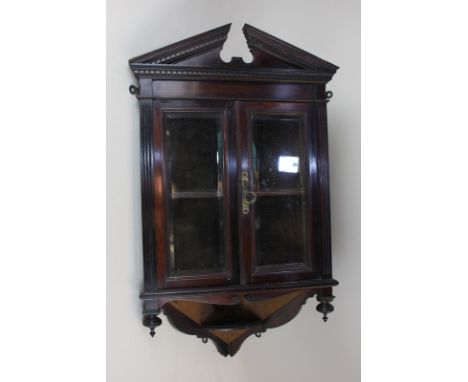 A small mahogany hanging corner wall cupboard with broken pediment above two glazed panel doors enclosing a single shelf, 40c