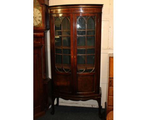 A George III mahogany glazed bow-front cabinet with twin arched panelled glazed doors enclosing four shelves, the lower shelf