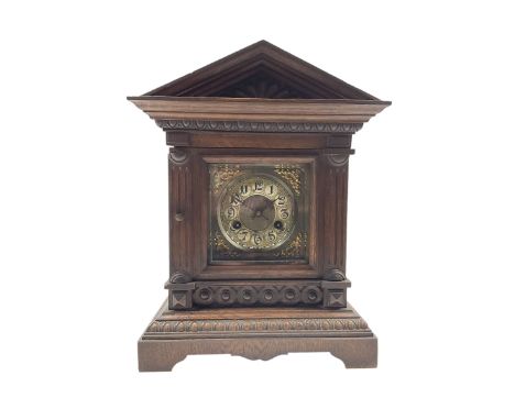 A German oak cased striking mantle clock with an architectural pediment, carved pilasters, shaped plinth and carved decoratio