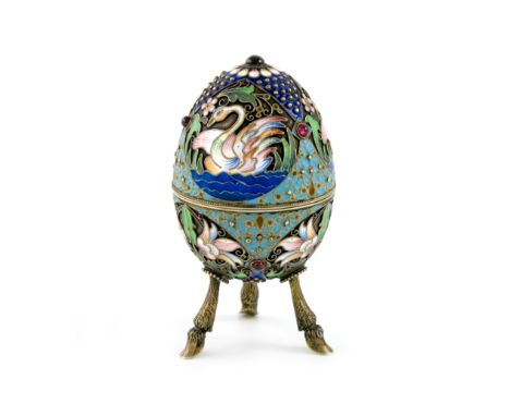 A Russian silver-gilt and enamel egg, enamelled with swans and foliate decoration within rope-work borders, set with red ston