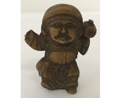 A carved Japanese netsuke in the shape of an oriental gentleman in robes holding a mallet.  Some damage to one hand. 