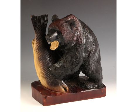 A Japanese carved wood model of a bear, 20th century, modelled with a fish in its paws, standing on a rectangular plinth base