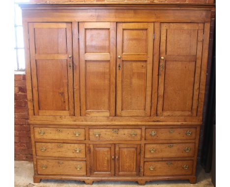 A George III honey oak housekeepers cupboard, the moulded cornice over an arrangement of four panelled cupboard doors, enclos