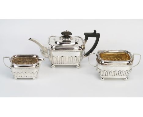 A matched three-piece Victorian silver three-piece tea service of rectangular outline with half-reeded decoration raised on b