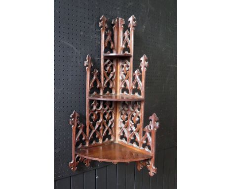 A Gothic revival mahogany corner shelf,  with pierced spire and fleur d'lys decorated back having three graduated semi-round 