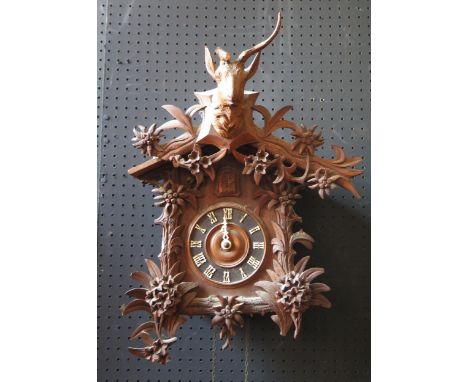 A Black Forest cuckoo clock, of traditional design the arched roof  surmounted by a stags head, with floral decoration to the