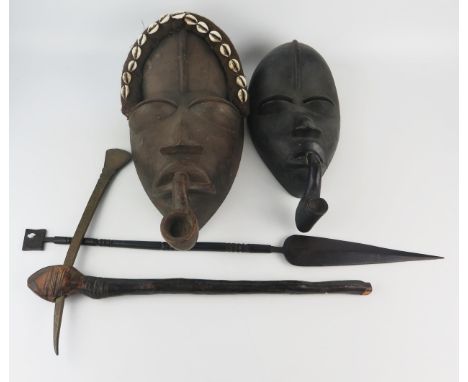 A Dan tribal carved wood mask with applied cowrie shell decoration, with a pipe in its mouth, 44cm high, together with anothe