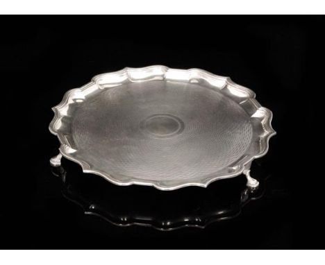 An Edwardian hallmarked silver circular salver of engine turned design within raised pie crust border, raised on three pad fe