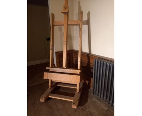 A beech adjustable studio easel with H frame ftted with base drawer on sled supports resting on casters. With detachable wind