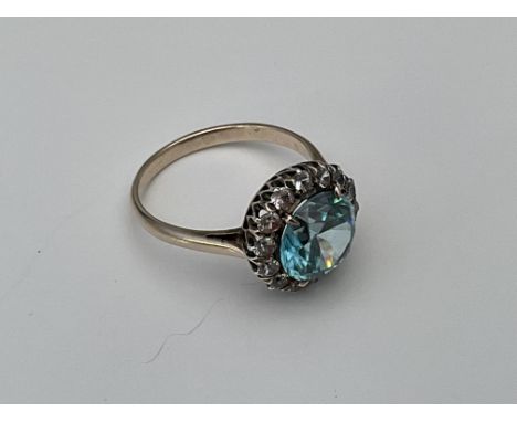 An unmarked ring set with a a halo of blue and white stones. Approx 3.3g, N.