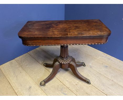 Regency figured mahogany pedestal fold over oblong card/tea table on reeded quadruped swept legs to brass caps and casters.  