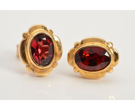 A PAIR OF GARNET STUD EARRINGS, each designed as a central oval garnet in a collet setting within a scalloped surround, butte