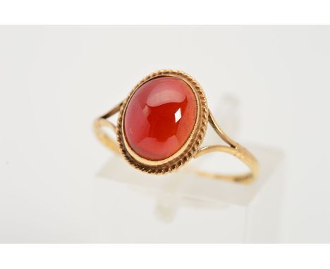A 9CT GOLD GEM RING, designed as a central oval red gem cabochon within a collet setting and rope twist surround to the bifur