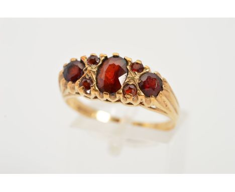 A 9CT GOLD GARNET RING, designed as a central oval garnet flanked by a circular garnet interspaced by four small circular gar