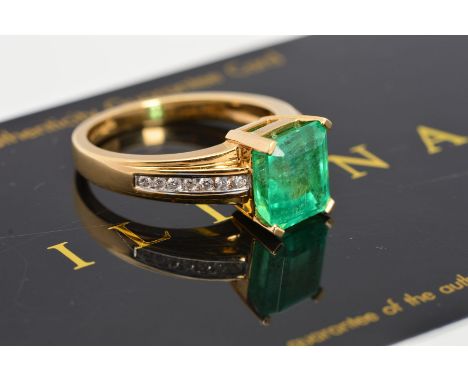 AN 18CT GOLD EMERALD AND DIAMOND RING, the central rectangular emerald within a four claw setting to the channel set diamond 