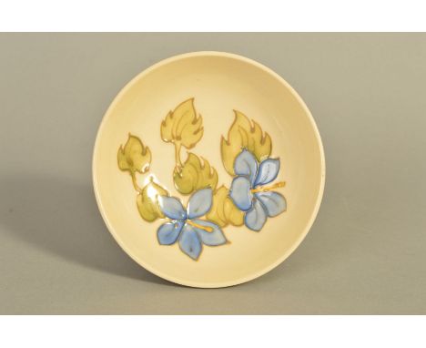 A MOORCROFT POTTERY FOOTED TRINKET DISH 'Blue Geranium' pattern on cream ground, impressed marks to base, diameter 11.5cm