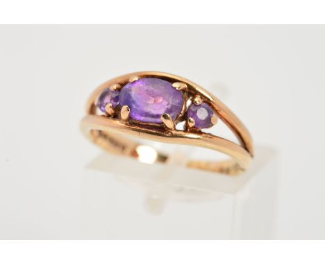 A 9CT GOLD AMETHYST RING, designed as a central oval amethyst flanked by circular amethysts to the bifurcated shoulders, with