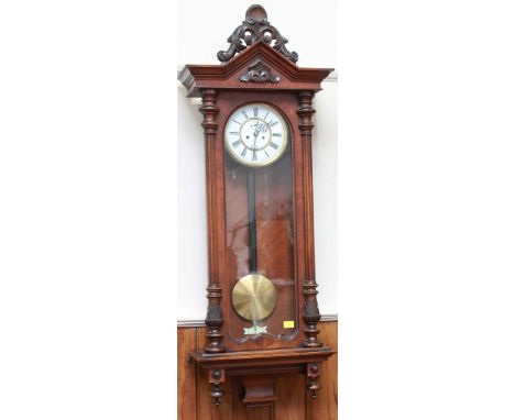A Victorian walnut Vienna wall clock with carved finial, the case with column sides, white circular dial with black Roman num