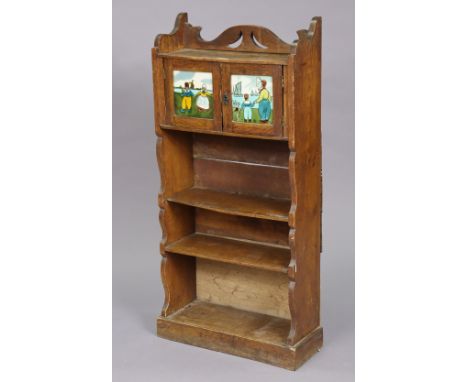 An Edwardian oak small standing open bookcase with a cupboard to top enclosed by a pair of doors each inset with a pictorial 