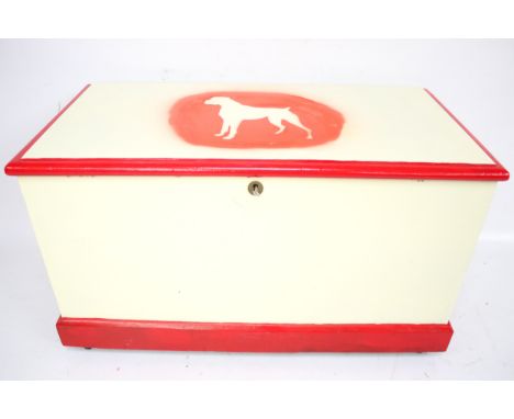 A vintage wooden blanket box. Painted cream with red edges and the outline of a dog on the lid, on casters, H59.5cm x W105cm 