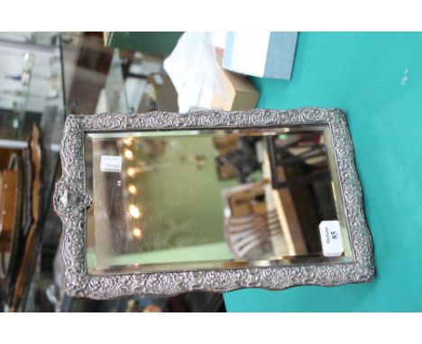 AN ANTIQUE SILVER FRAMED EASEL BACKED MIRROR with scrolling foliate decoration, makers mark indistinct above the bevelled edg