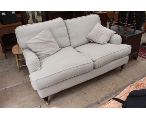 A STONE GREY COLOURED TWO SEATER SOFA with shaped back and standing on turned legs terminating in brass casters, 161cm x 74cm