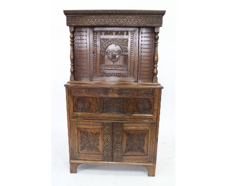 AN ANTIQUE OAK CUPBOARD with a single door above a fall front and two doors, all with carved decoration and raised on bracket