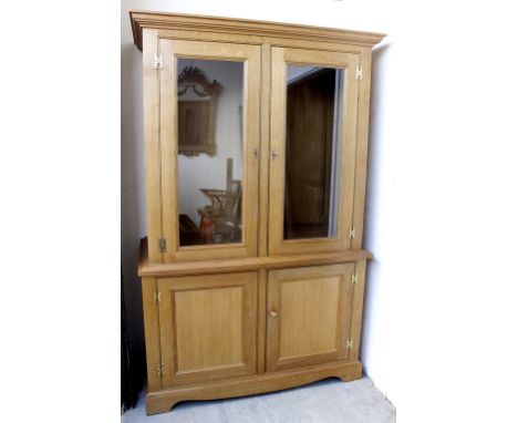 A LIGHT OAK CUPBOARD with twin glazed doors above twin panelled doors, raised on bracket feet, 130cm wide x 65cm deep x 204cm