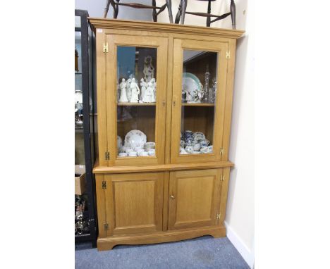 A LIGHT OAK CUPBOARD with twin glazed doors above twin panelled doors, raised on bracket feet, 134cm wide x 66cm deep x 204cm