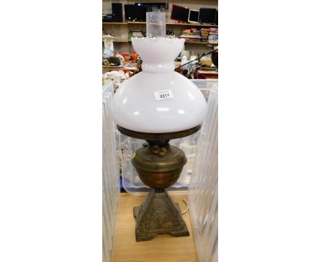 A brass oil lamp, with a milk glass shade, brass central reservoir on a floral decorated base, converted to electricity, 57cm