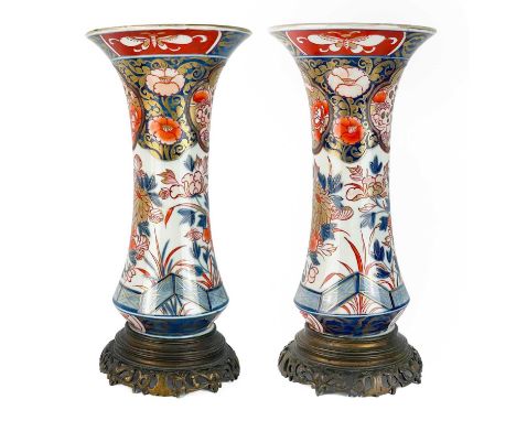 A pair of Japanese Imari trumpet vases, Meiji period. Each with an attached gilt metal stand, opposing dog of fo cartouches a