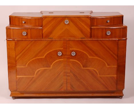 An Art Deco figured walnut cocktail sideboard, having a twin hinged fitted central compartment with interior mirror, flanked 