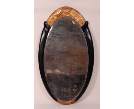 An Art Deco period ebonised pine oval framed wall mirror, having upper and lower floral gilt carved detail, 134 x 79cm Condit