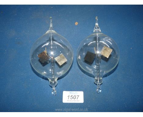 Two hand-blown glass Spheres with hanging loops and containing light driven rotors, 5 1/4'' long approx.