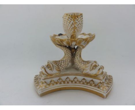 An early 19th century cream ground candlestick of trefoil shaped form supported by three stylised dolphins, with moulded shel