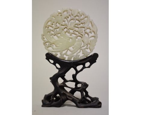 A Chinese carved and pierced celadon jade roundel, decorated with a phoenix, 7.5cm diameter, on carved and pierced hardwood s