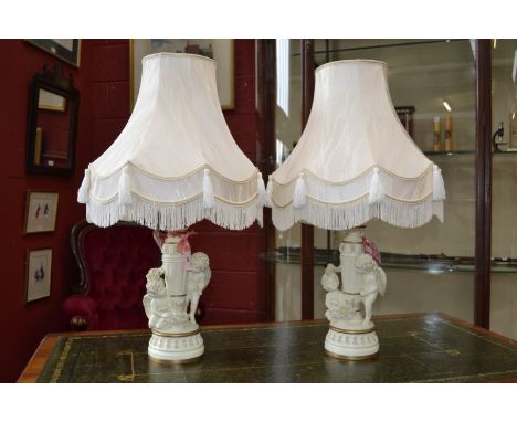 A pair of cream and gilt ceramic table lamps moulded as cherubs framing a fluted vasular column, shades en suite.