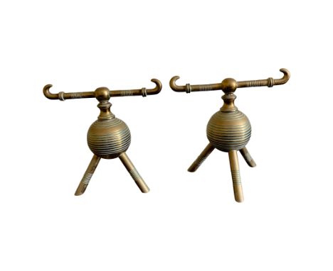 A pair of brass fire dogs designed by Christopher Dresser each with horned rest, ribbed sear and three banded legs, maximum h