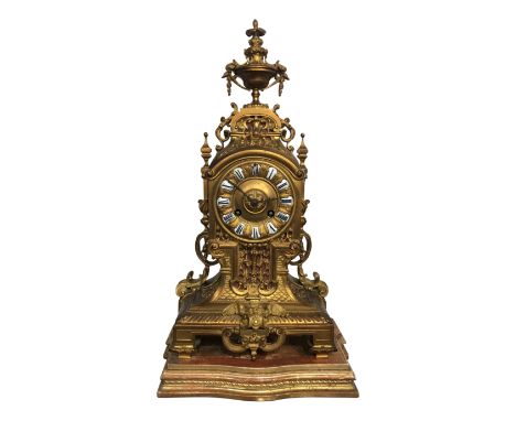 An ornate gilt-metal mantle clock, with white enamel dials, together with an associated carved giltwood stand and key, 40.5cm