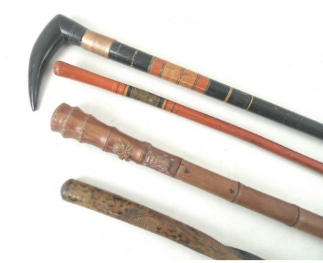 A group of sticks containing a modern wooden walking cane, carved to look like bamboo, with three insects carved to the handl