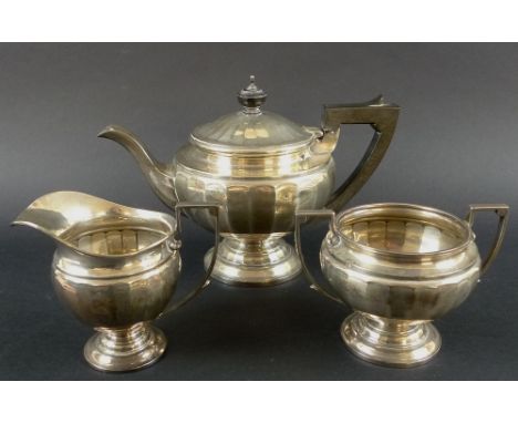 An early Art Deco silver tea service of fluted form, comprising a teapot with pedestal base, ebony handle and finial, creamer