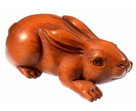A JAPANESE CARVED AND STAINED WOOD NETSUKE IN THE FORM OF A CROUCHING HARE, 5CM L, SIGNED