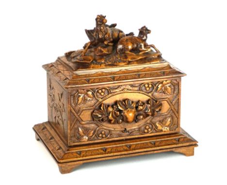 A late 19th Century Black Forest carved wooden cigar box
The hinged lid and front panel featuring two recumbent sheep on natu