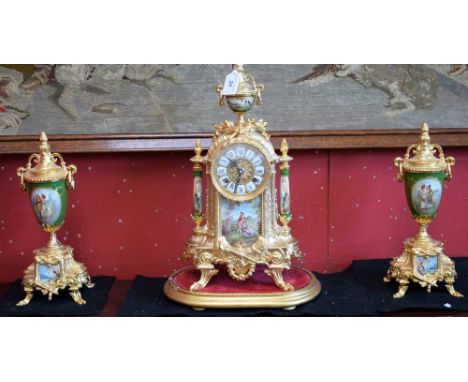 An ornate clock garniture, in the French style, gilt metal, emerald green ceramic urns and columns, panels depicting courting