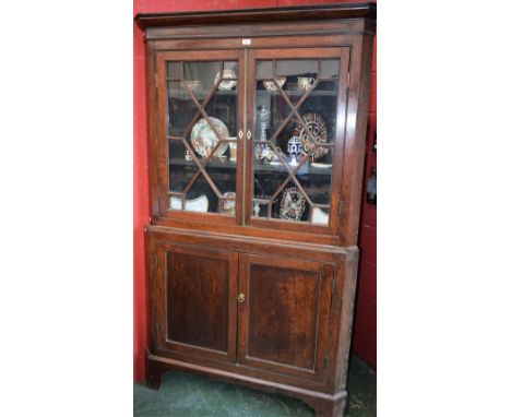 A 19th century oak corner display cabinet, outswept cornice above a pair of astragal glazed doors enclosing two shelves, the 