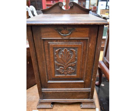 An early 20th century oak purdonium, moulded top above a fall front panel door, applied with a foliate motif, enclosing a rem